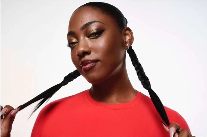 A dark-skinned woman poses with braided hair and red shirt against a white background, showcasing beauty and fashion elements.