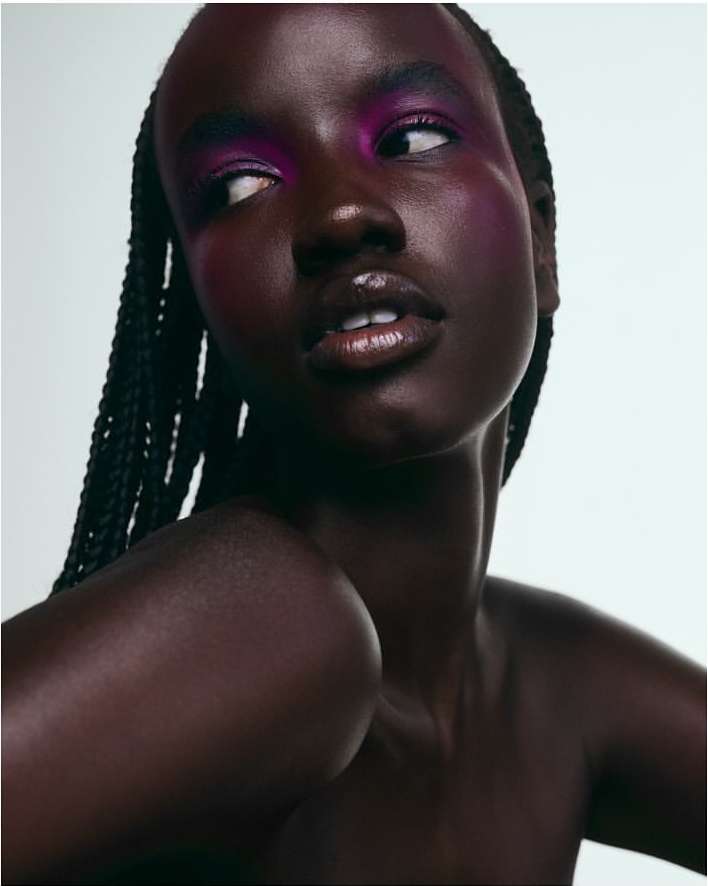 Close-up portrait of a Black woman with braided hair and vivid pink eyeshadow looking away against a white background