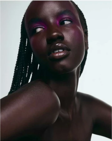 Close-up portrait of a Black woman with braided hair and vivid pink eyeshadow looking away against a white background