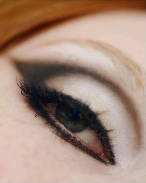 Close-up of a woman's eye with black eyeliner and mascara enhancing the eyelashes, set against a soft, blurred skin background.