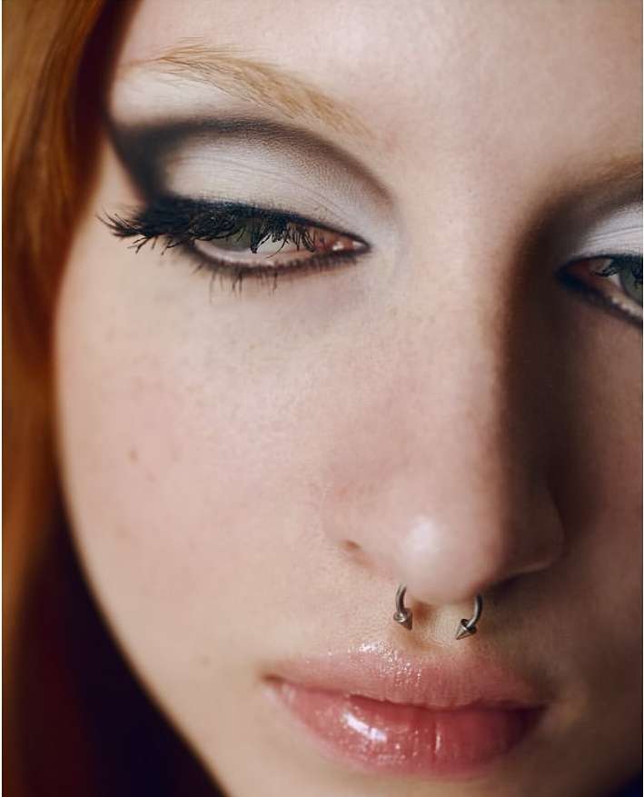 Close-up portrait of a young woman with fair skin, red hair, nose ring, and smokey eye makeup, focusing on beauty and personal expression.