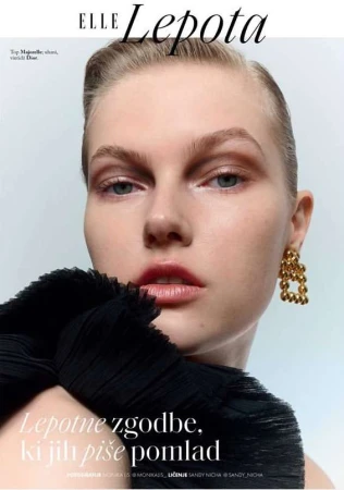 Close-up beauty portrait of a female model wearing chunky gold earrings and a textured black top against a light background.