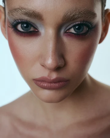 Close up portrait of a woman with dramatic eye makeup and bleached eyebrows photographed by Monika Lis
