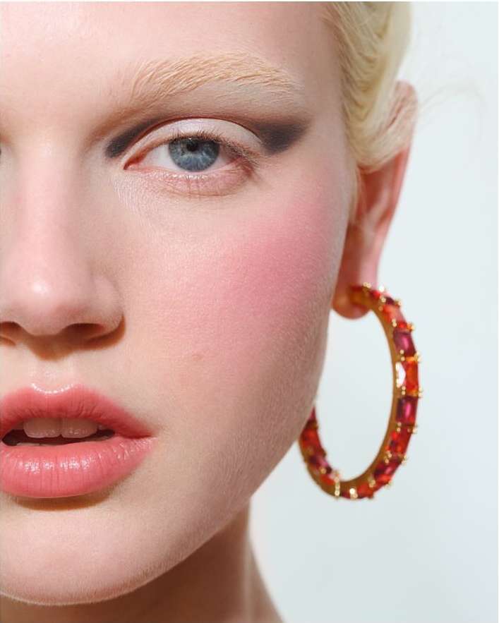 Close-up portrait of an adult female model with pale skin, wearing bright eye makeup, an earring, and looking at the camera.
