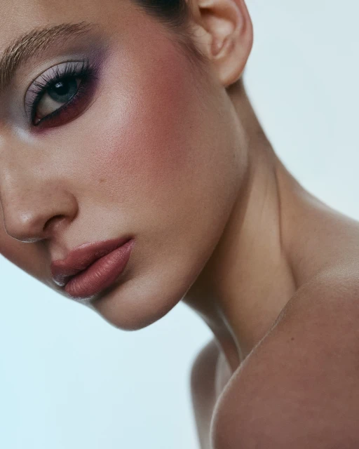 Close-up studio portrait of a woman showcasing colorful eye makeup and glossy lips against a light blue backdrop, beauty and fashion.