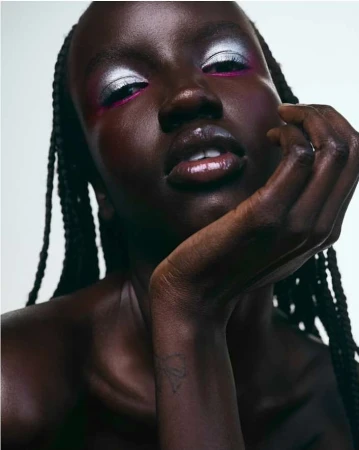 Close-up beauty shot of an African-descent woman with braided hair and silver and pink eyeshadow, against a light neutral backdrop.