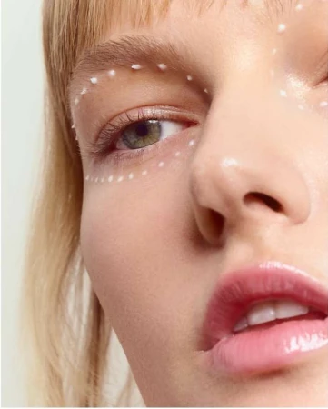 Close-up beauty portrait of a woman with white dotted makeup framing her eye and glossy pink lips.