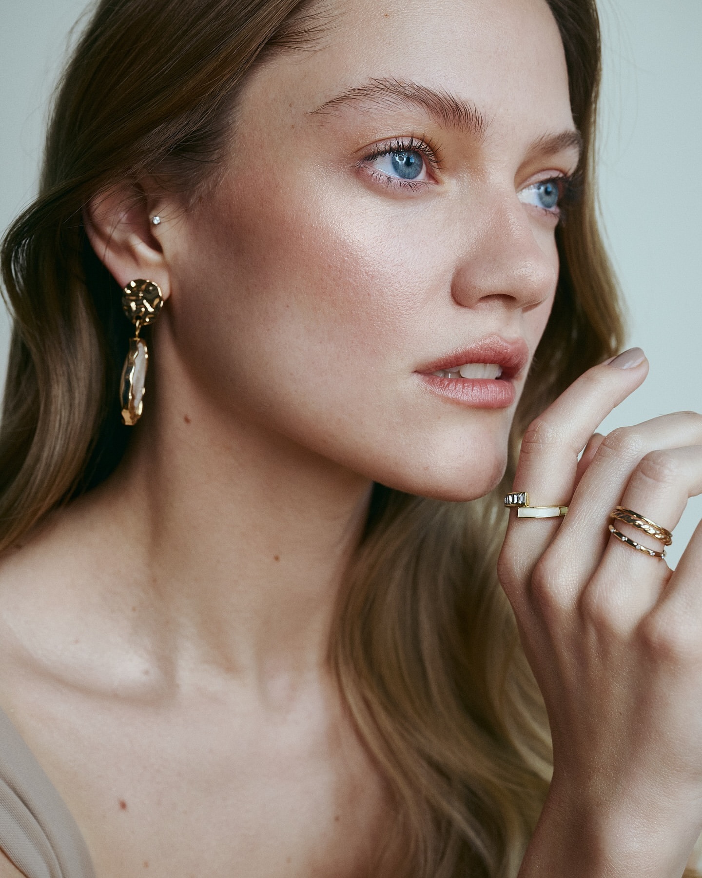 Close-up of an adult woman with fair skin and blonde hair wearing elegant gold jewelry. Beauty shot with a neutral background.