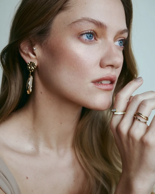 Close-up of an adult woman with fair skin and blonde hair wearing elegant gold jewelry. Beauty shot with a neutral background.