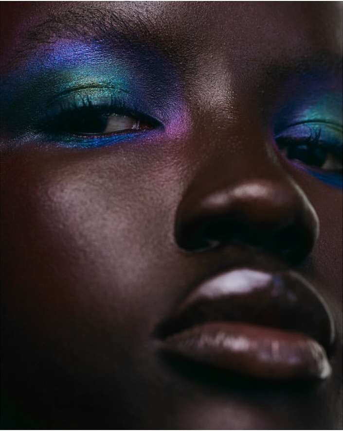 Close-up portrait of a Black woman featuring iridescent blue and purple eyeshadow and glossy lips by Monika Lis.