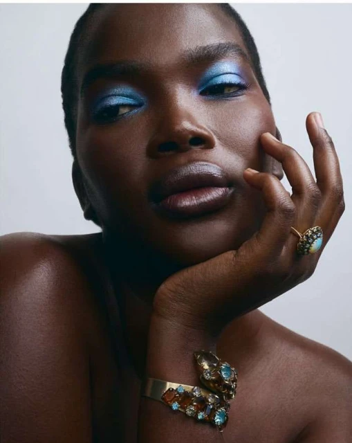 Close-up beauty shot of an African-American woman with blue eyeshadow, wearing a gold ring and a gem-encrusted serpent bracelet.