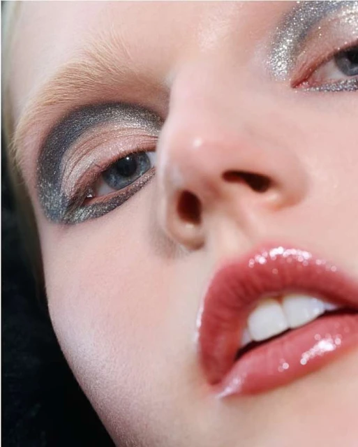 Close-up of a model's face with dramatic eye makeup and glossy lips in a beauty shot, displaying makeup artistry and facial features.