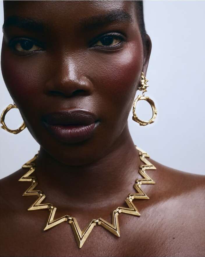 Close-up portrait of a Black woman wearing textured gold hoop earrings and a geometric gold statement necklace by Monika Lis