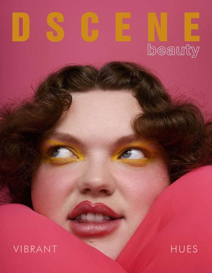 Magazine cover featuring a woman with vibrant yellow eye makeup and pink fabric framing her face against a matching pink background.