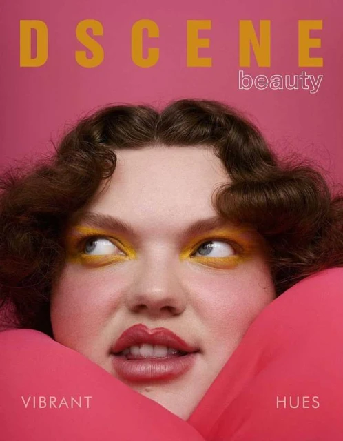 Magazine cover featuring a woman with vibrant yellow eye makeup and pink fabric framing her face against a matching pink background.