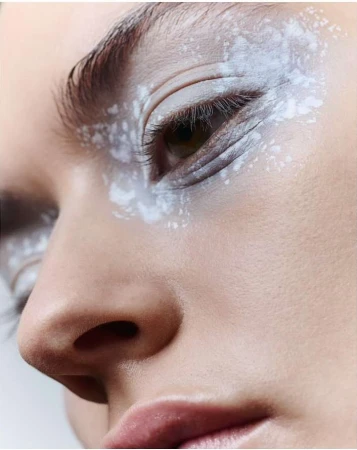 Close-up beauty portrait of a person with textured white pigment makeup around the eye area by Monika Lis