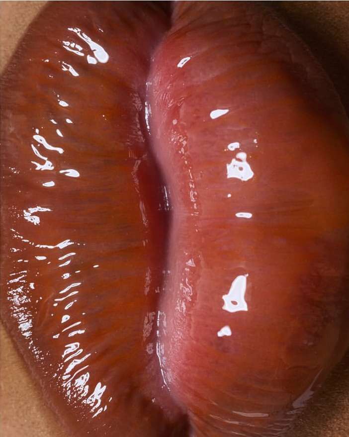 Close-up of glossy red lips showcasing texture and light reflections, detailed view of human facial feature, and beauty.