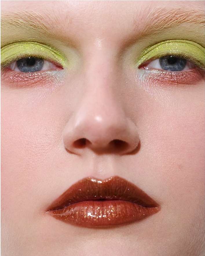 Extreme close-up of a model with iridescent lime green eyeshadow and glossy brown lips. Fashion and beauty makeup concept.