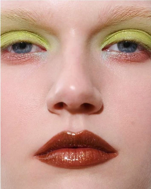 Extreme close-up of a model with iridescent lime green eyeshadow and glossy brown lips. Fashion and beauty makeup concept.