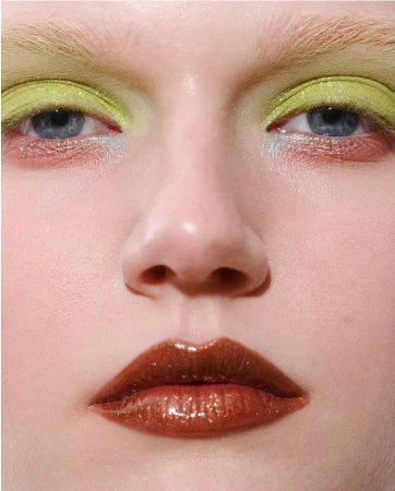 Extreme close-up of a model with iridescent lime green eyeshadow and glossy brown lips. Fashion and beauty makeup concept.
