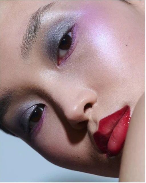 Close-up portrait of an Asian adult female with iridescent eyeshadow and glossy red lips, showcasing a beauty and fashion concept.