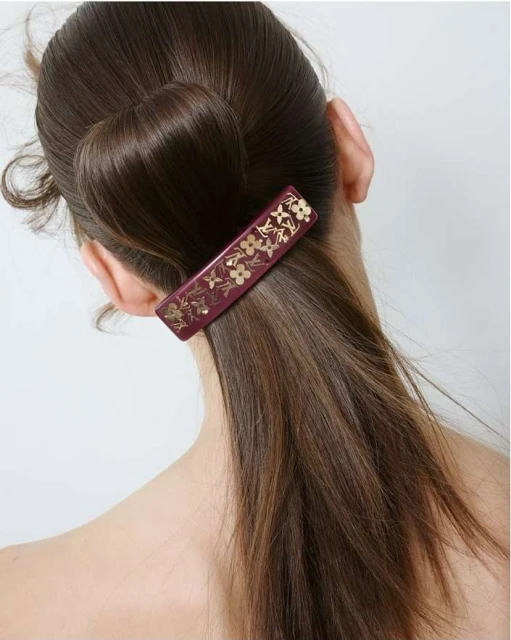 Close-up of a brunette woman's hair styled with a burgundy and gold floral hair clip, showcasing an elegant and fashionable accessory.