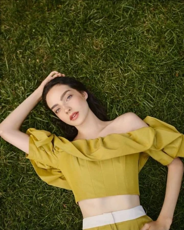A woman lying down on green grass wearing an off-the-shoulder yellow top, captured from a high-angle overhead perspective.