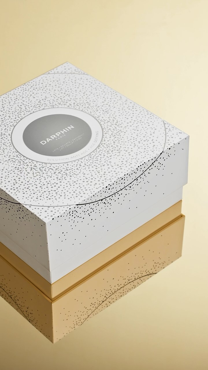 Darphin skincare product box in white with gold accents on a gold reflective background. Cosmetics and beauty packaging.