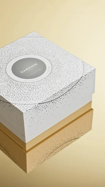 Darphin skincare product box in white with gold accents on a gold reflective background. Cosmetics and beauty packaging.