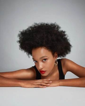 Close-up portrait of a Black woman with an afro wearing a black top and red lipstick against a plain grey background