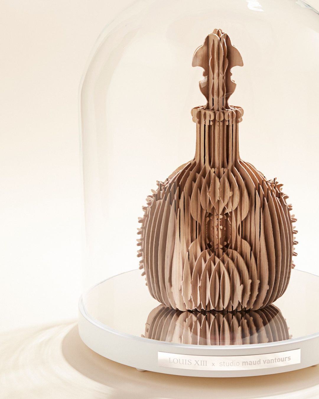 Artistic photograph of a wooden bottle sculpture under a glass dome on a white platform, showcasing intricate design in a minimalist setting.