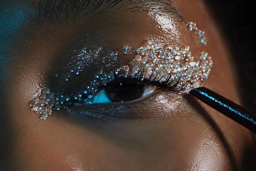 Close-up on a person's eye with artistic makeup featuring small, clear beads and blue accents, highlighting beauty and creative expression.