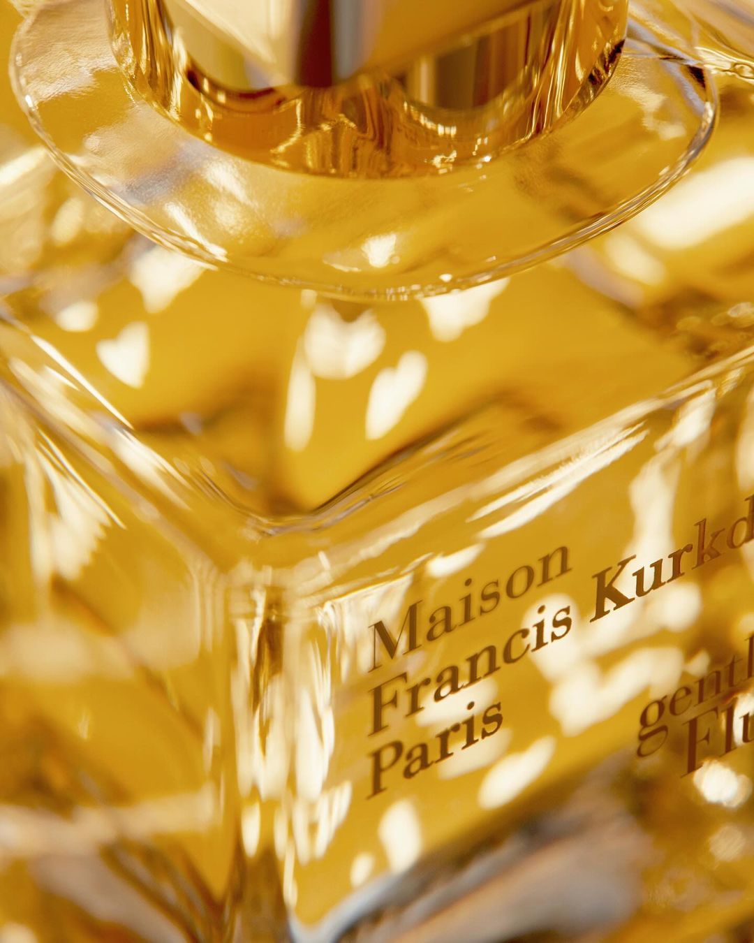Close-up of a square-shaped glass perfume bottle with gold accents, showcasing the brand 'Maison Francis Kurkdjian Paris'.