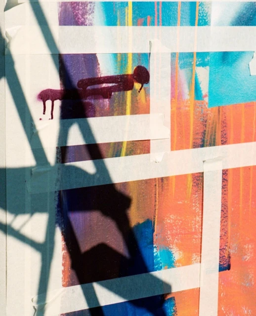 Abstract artwork featuring paint splatters and masking tape, showcasing a blend of orange, blue, and purple hues, alongside geometric shapes.