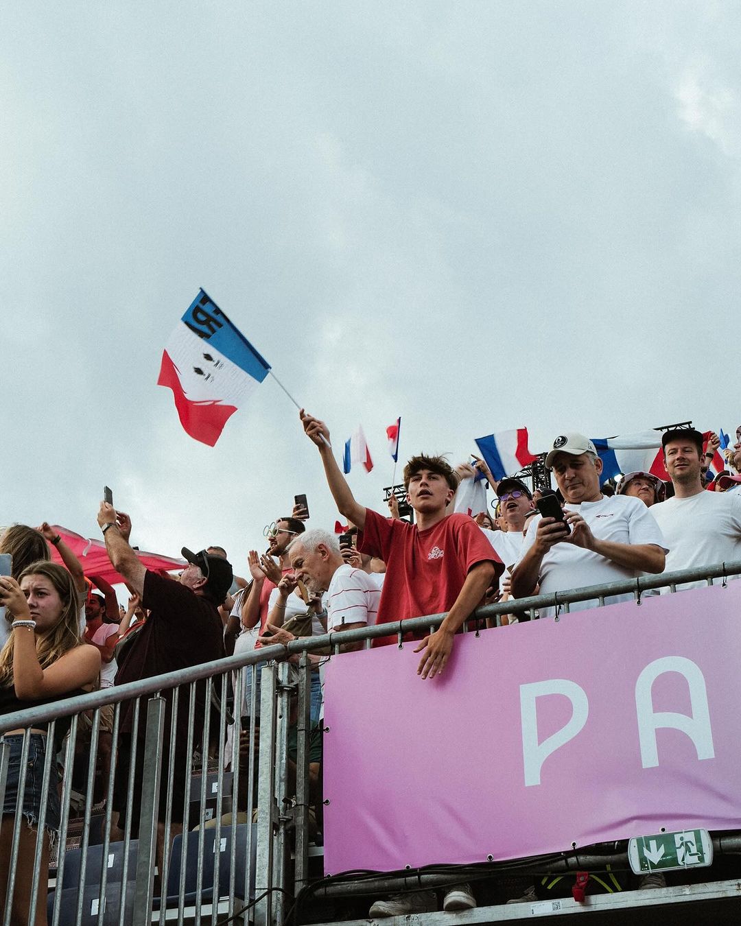 Enthusiastic crowd with French flags, capturing a dynamic scene of people enjoying an event outdoors in daylight under an overcast sky.