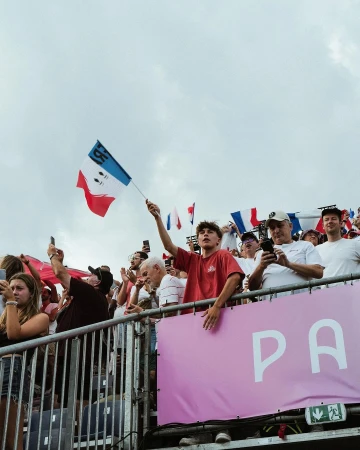 Enthusiastic crowd with French flags, capturing a dynamic scene of people enjoying an event outdoors in daylight under an overcast sky.