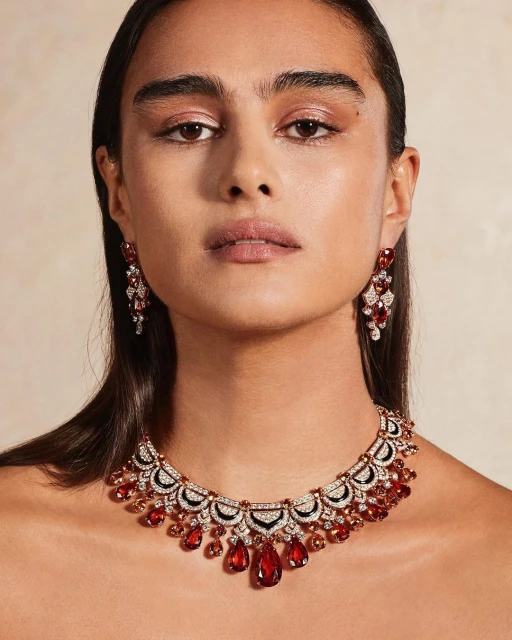 Close-up shot of a woman wearing a red and white gemstone necklace and matching earrings against a neutral background.