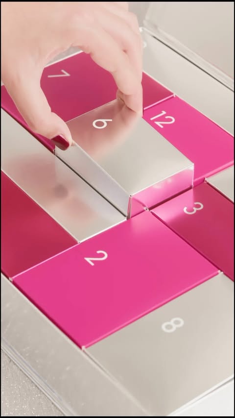 Close-up of a hand opening a silver and pink advent calendar numbered with white text for the holiday or seasonal celebration.