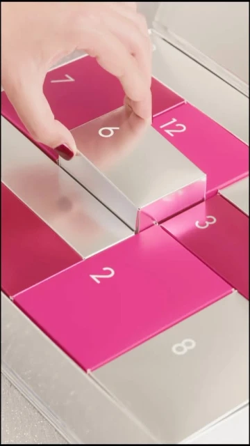 Close-up of a hand opening a silver and pink advent calendar numbered with white text for the holiday or seasonal celebration.