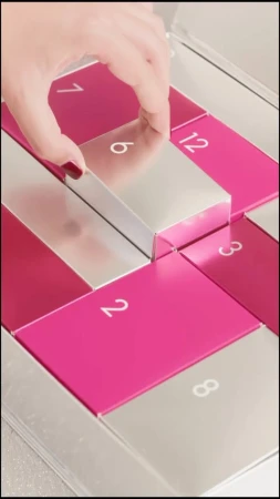Close-up of a hand opening a silver and pink advent calendar numbered with white text for the holiday or seasonal celebration.