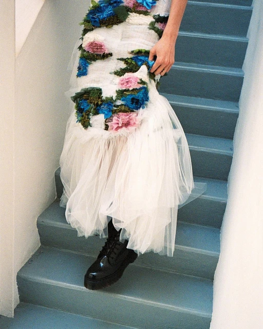 Person in a floral-embellished dress and platform boots descending a set of blue stairs in an indoor setting with natural lighting.