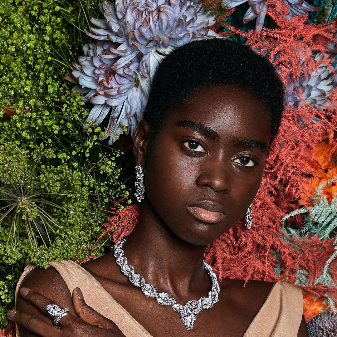 Portrait of a black woman wearing a diamond necklace and earrings surrounded by vibrant flowers