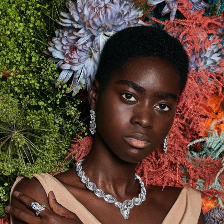 Portrait of a black woman wearing a diamond necklace and earrings surrounded by vibrant flowers