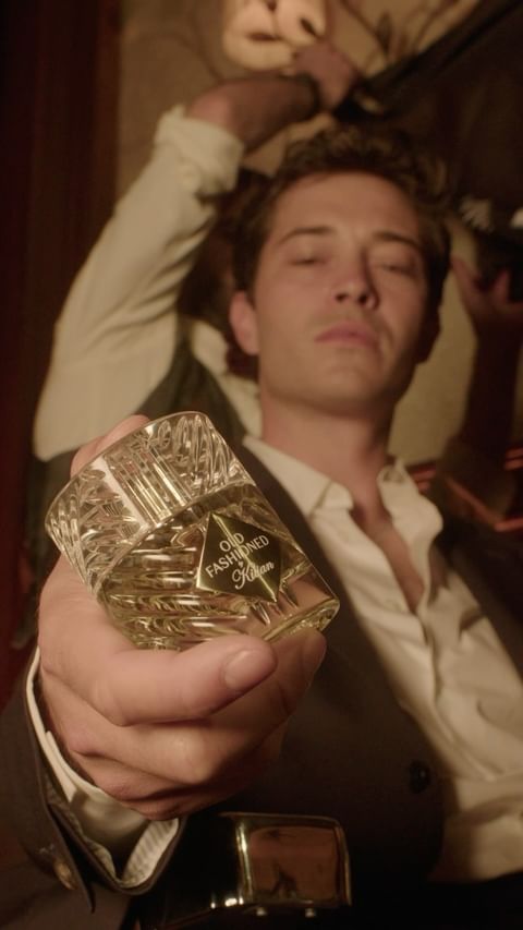 Portrait of a man with a suit jacket holding a crystal-cut perfume bottle in hand with an old fashioned label, indoors.