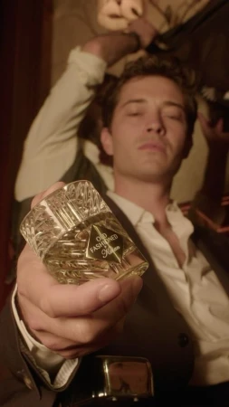 Portrait of a man with a suit jacket holding a crystal-cut perfume bottle in hand with an old fashioned label, indoors.