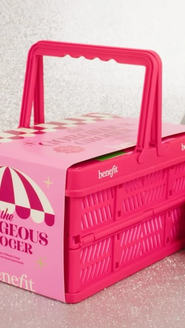 Bright pink Benefit Cosmetics gift set in a picnic basket-style container with packaging and festive glitter background, product shot.