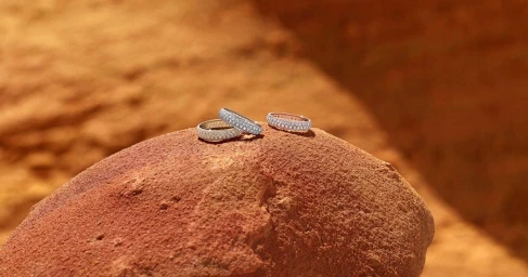 Three diamond pave eternity rings resting on a rough red rock surface in an outdoor desert landscape.
