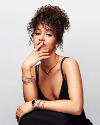 Portrait of a woman with curly hair wearing a black top and gold jewellery against a light background by Monsieurtok
