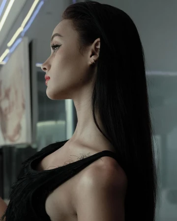 Profile portrait of a woman with long black hair wearing a black sleeveless top against an indoor interior background.