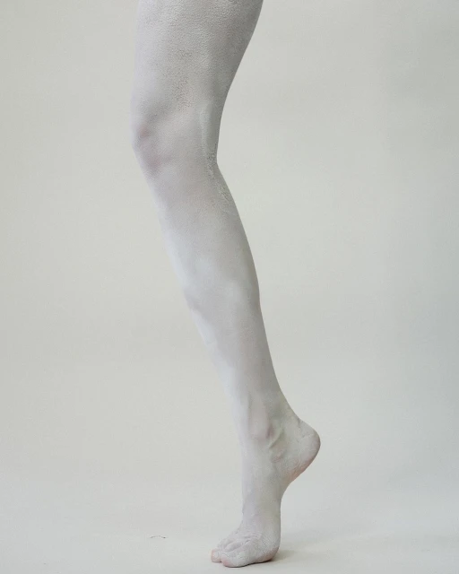 A close-up studio shot shows the lower half of an adult female covered in white paint standing against a neutral off-white background.